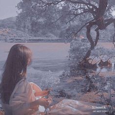 a woman sitting under a tree on top of a blanket