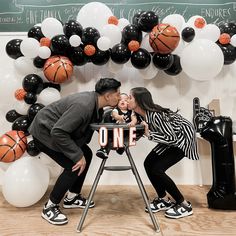 a man and woman kissing while holding a baby in front of a basketball themed backdrop