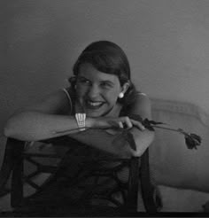 black and white photograph of a smiling woman sitting on a chair with her arm crossed