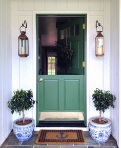 two potted plants are sitting on the front step of a house with green doors