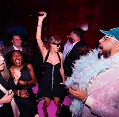 a group of people at a party with one woman in a dress and the other man in a feather boa