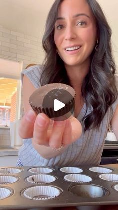 a woman holding up a chocolate cupcake in front of a muffin tins