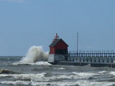 a lighthouse in the middle of some rough ocean water with waves crashing against it and people standing on the pier