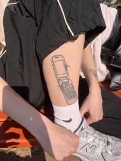 a person with a cell phone tattoo on their leg, sitting next to a bench