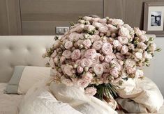 a large bouquet of pink roses on top of a bed with white sheets and pillows