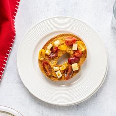 a white plate topped with a doughnut covered in fruit and nuts next to a glass of water