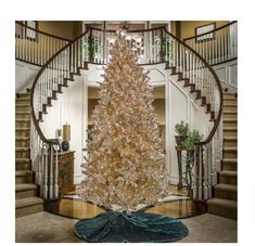 a white christmas tree sitting in the middle of a living room next to a spiral staircase