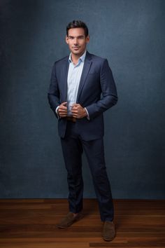 a man in a suit and tie standing on a wooden floor with his hands in his pockets