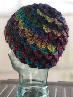 a multicolored crocheted hat sitting on top of a clear glass vase