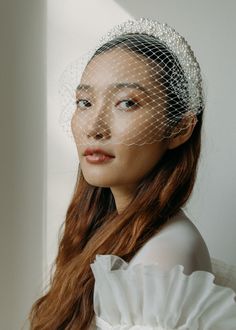 a woman wearing a veil and headpiece with long red hair in front of a white wall