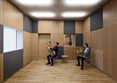 two people sitting on chairs playing instruments in a room with wood paneled walls and flooring