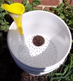 a white bucket with a yellow spoon in it sitting on the ground next to some plants