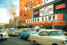 an old photo of cars parked in front of a movie theater with neon signs on the building