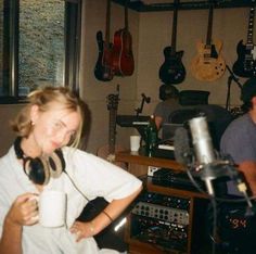 a woman holding a coffee cup in front of a recording studio with guitars on the wall