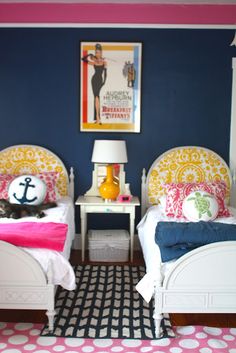 two twin beds in a room with polka dot flooring and blue walls, one has an anchor pillow on the end table