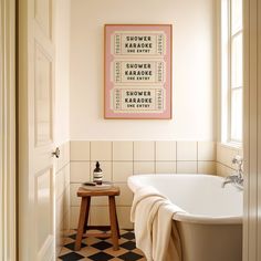 a white bath tub sitting next to a wooden stool in a bathroom under a framed poster