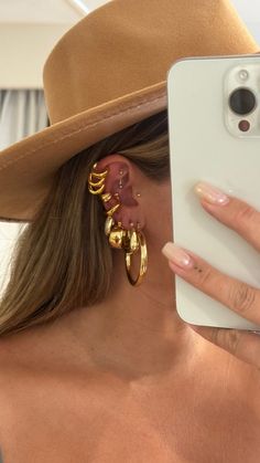 a woman in a brown hat is taking a selfie with her cell phone and wearing gold earrings