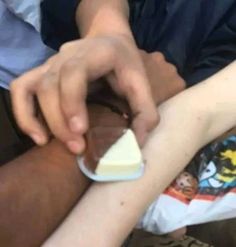 a person holding onto a piece of cake on top of someone's arm while sitting down