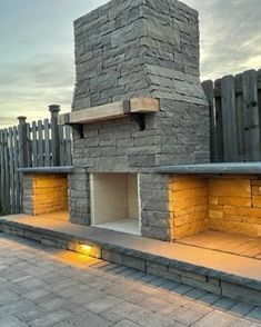 an outdoor fireplace is lit up with yellow lights on the side and in front of a wooden fence