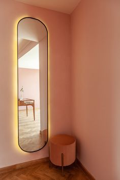 a pink room with a round mirror on the wall and a stool in front of it