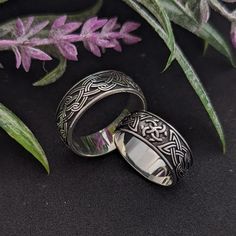 two silver rings sitting next to each other on top of a black surface with purple flowers in the background