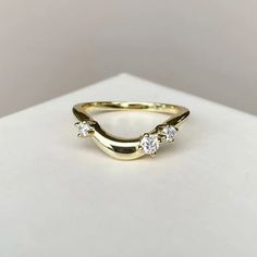 a yellow gold ring with three diamonds on the top and bottom, sitting on a white surface