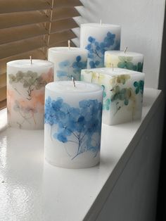 four candles with flowers painted on them sitting on a window sill