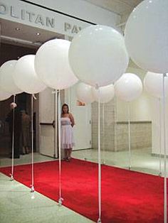 a woman standing in front of a red carpeted hallway with white balloons on the floor