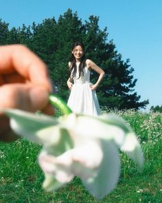 a woman in a white dress is holding a flower with her hand and looking at the camera