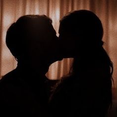 the silhouette of two people kissing each other in front of a curtained window with curtains behind them