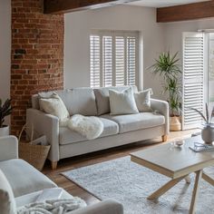 a living room with brick walls and white furniture in the center, along with large windows that have shutters on them