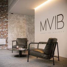 two chairs and a table in front of a wall with the m v b logo on it