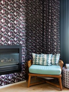 a chair and ottoman in front of a wall with a patterned pattern on it, next to a fire place