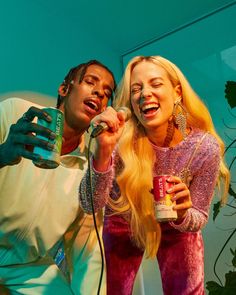 two people standing next to each other holding cans and singing into a microphone while one person holds a can