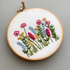 a close up of a embroidery on a hoop with flowers in the center and leaves around it