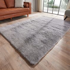 a living room with a couch, chair and rug on the hardwood floor in front of a sliding glass door