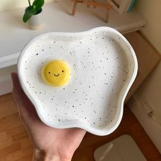 a hand holding a white bowl with an egg in the shape of a smiley face