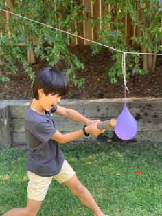 a young boy swinging a bat at a purple ball on a string in the yard