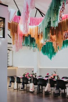 a room filled with tables and chairs covered in colorful streamers hanging from the ceiling