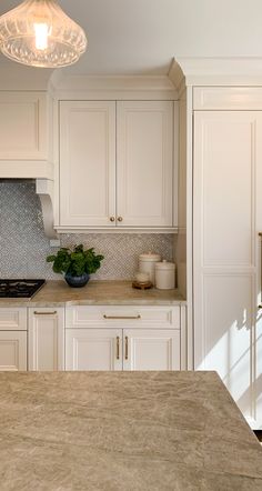 a kitchen with marble counter tops and white cabinets, along with a light hanging over the stove