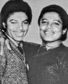 two young men standing next to each other in front of a white wall and smiling at the camera