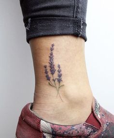 a small lavender flower tattoo on the side of a woman's lower leg and ankle