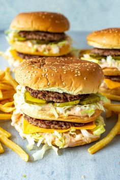 three hamburgers with cheese, pickles and lettuce sitting on top of french fries