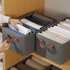 the woman is holding two bins with folded clothes in them and reaching for one