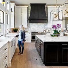 a woman standing in the middle of a kitchen with black cabinets and white countertops