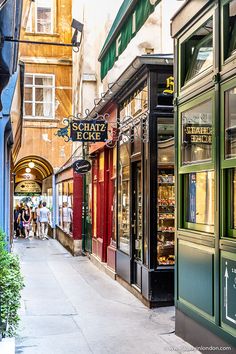 an alley way with shops and people walking down the sidewalk in front of them on a sunny day