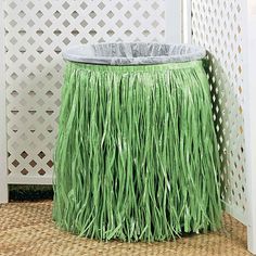 a green grass skirt sitting on top of a wooden floor next to a white fence