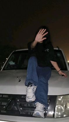 a man sitting on the hood of a white car with his hands in the air