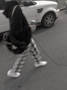 a person walking down the street in front of a white car with a black hoodie on