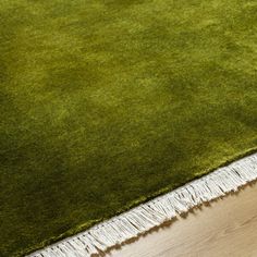 a green rug with white fringes on top of it and a wooden floor in the background